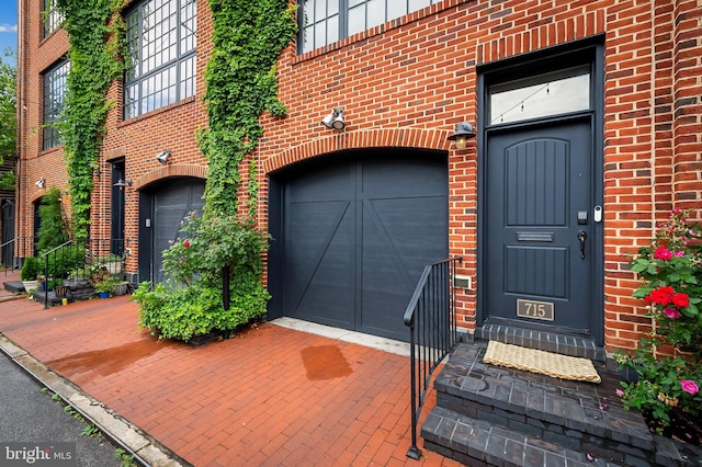 view of exterior entry featuring a garage, decorative driveway, and brick siding