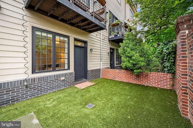 entrance to property with brick siding, a balcony, and a yard