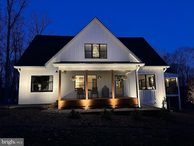 back of house at night featuring a porch and board and batten siding