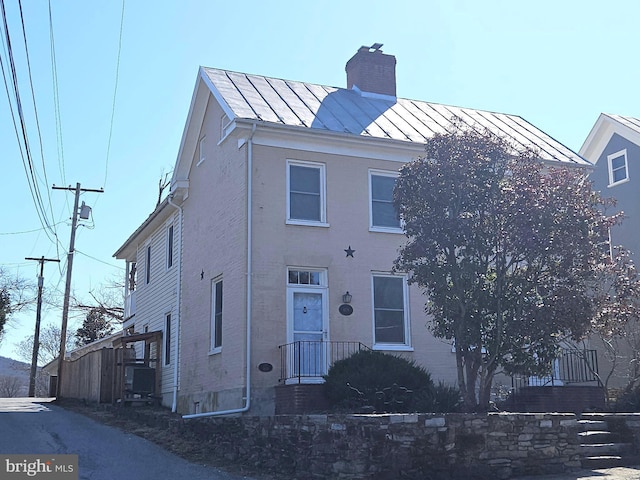 view of front facade with metal roof, a chimney, and a standing seam roof