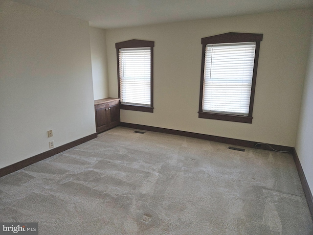 spare room with light carpet, visible vents, and baseboards