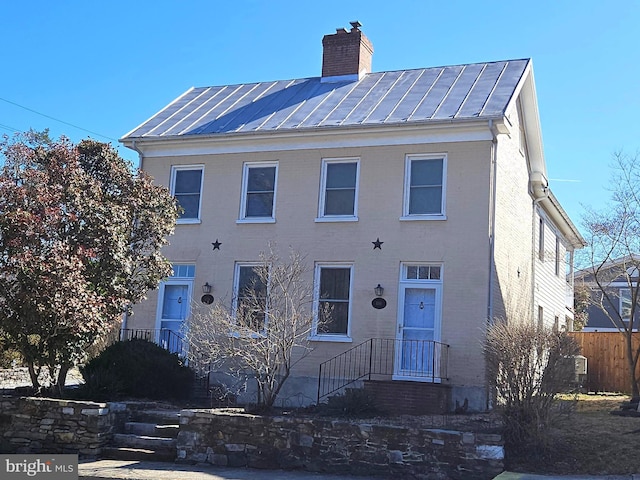 view of front of property featuring fence, a standing seam roof, a chimney, brick siding, and metal roof