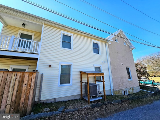 rear view of property with a balcony, central air condition unit, and fence