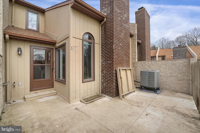 view of side of home featuring fence, roof with shingles, central AC, a chimney, and a patio area