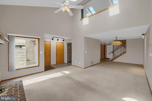 unfurnished living room with ceiling fan, stairway, light colored carpet, a skylight, and a towering ceiling