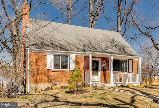 cape cod home with brick siding, covered porch, a chimney, and a front yard