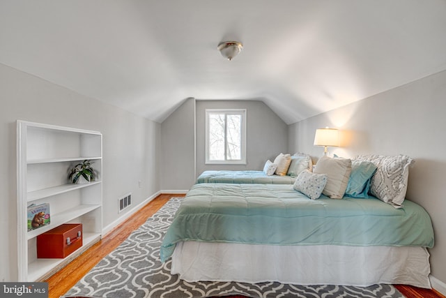 bedroom featuring visible vents, baseboards, wood finished floors, and vaulted ceiling