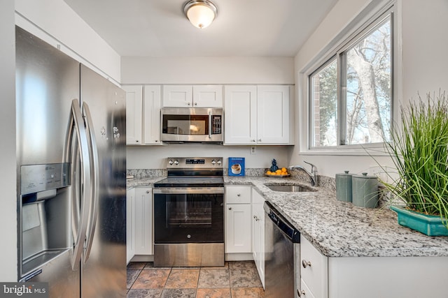 kitchen featuring stone finish flooring, light stone countertops, white cabinets, stainless steel appliances, and a sink