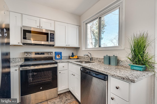 kitchen with a sink, light stone counters, appliances with stainless steel finishes, and white cabinetry