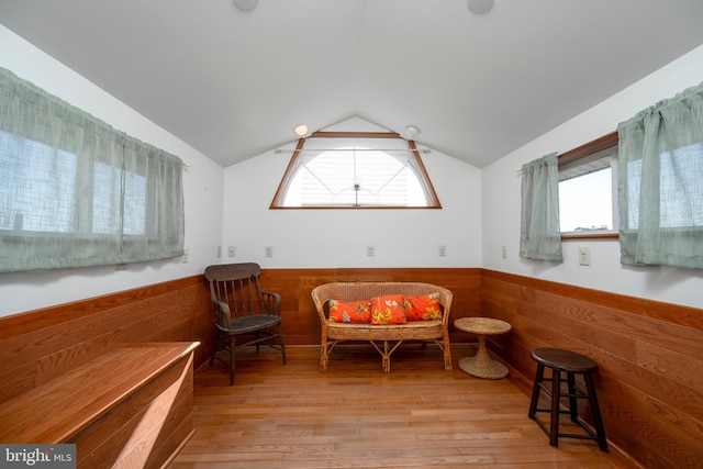 living area featuring a wainscoted wall, wood finished floors, wood walls, and vaulted ceiling