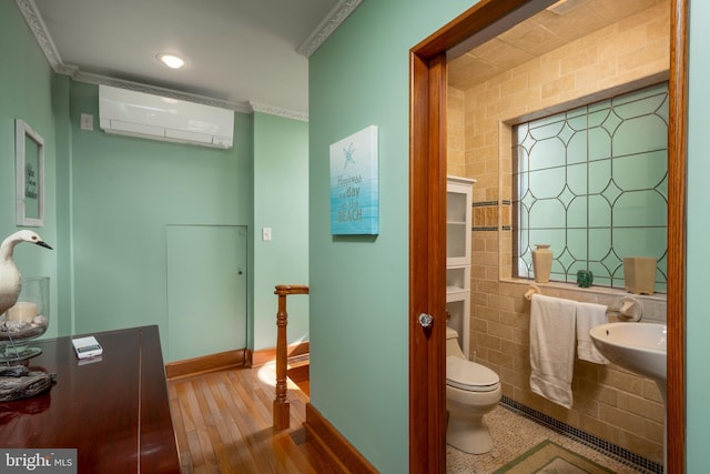 bathroom featuring wood finished floors, a wall mounted AC, a sink, tile walls, and toilet