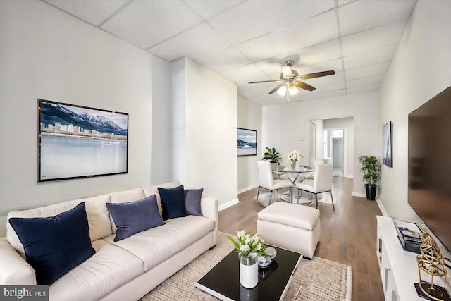 living area with ceiling fan, a drop ceiling, baseboards, and wood finished floors