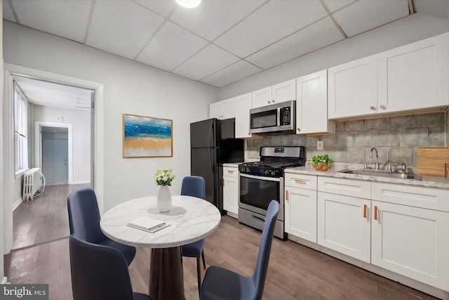 kitchen with backsplash, radiator, appliances with stainless steel finishes, dark wood-style floors, and a sink