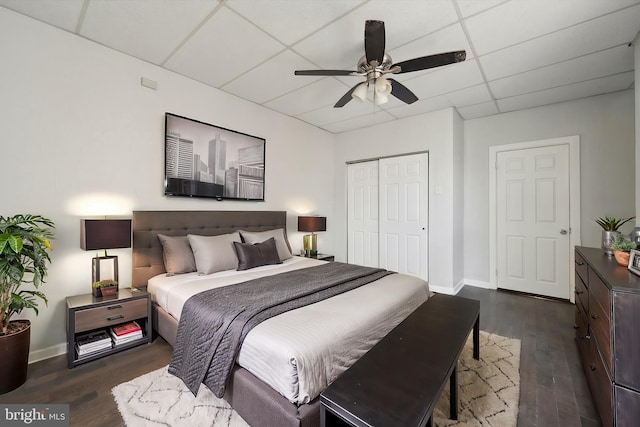 bedroom with a drop ceiling, baseboards, a closet, and dark wood finished floors