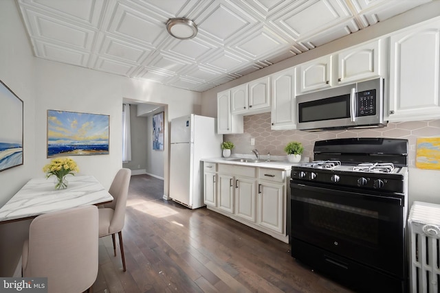 kitchen with black gas range oven, stainless steel microwave, freestanding refrigerator, an ornate ceiling, and a sink