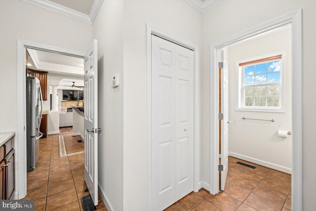 hall featuring light tile patterned floors, visible vents, baseboards, and ornamental molding