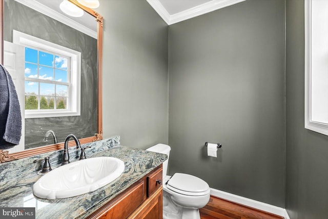 half bath with toilet, ornamental molding, wood finished floors, baseboards, and vanity