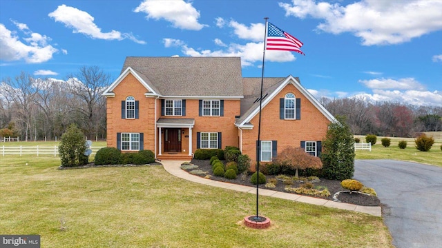 colonial-style house with brick siding, a front yard, and fence