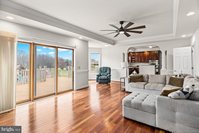 living room with a ceiling fan, a tray ceiling, arched walkways, hardwood / wood-style flooring, and crown molding