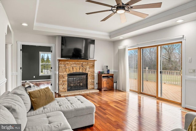 living area with ornamental molding, a ceiling fan, a tray ceiling, and hardwood / wood-style floors