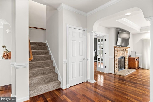 stairs with wood finished floors, crown molding, and ornate columns