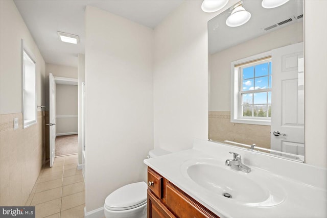 half bath featuring tile patterned floors, visible vents, toilet, tile walls, and vanity