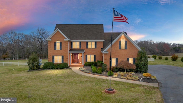 view of front of home with brick siding, a lawn, and fence