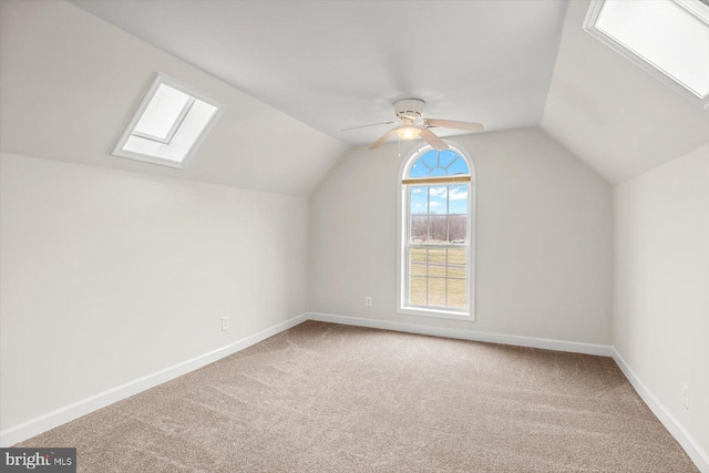 additional living space with vaulted ceiling with skylight, carpet, baseboards, and ceiling fan