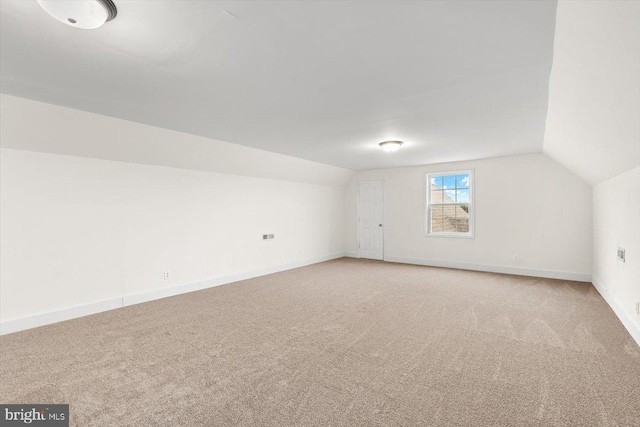 additional living space featuring vaulted ceiling, light colored carpet, and baseboards