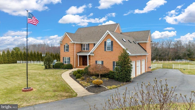 traditional-style house with fence, driveway, roof with shingles, a front lawn, and brick siding