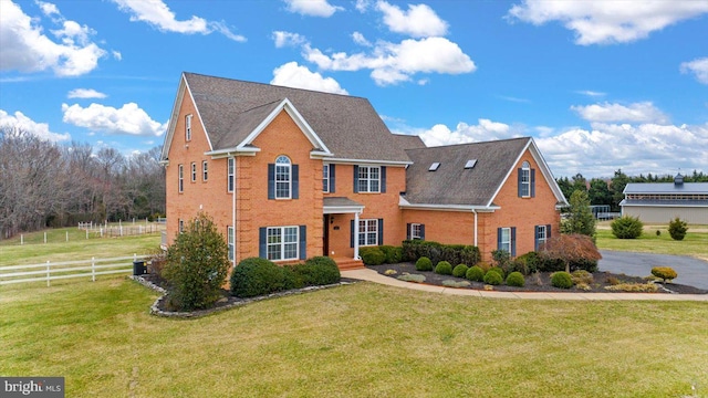 view of front facade with brick siding, central air condition unit, a front yard, and fence