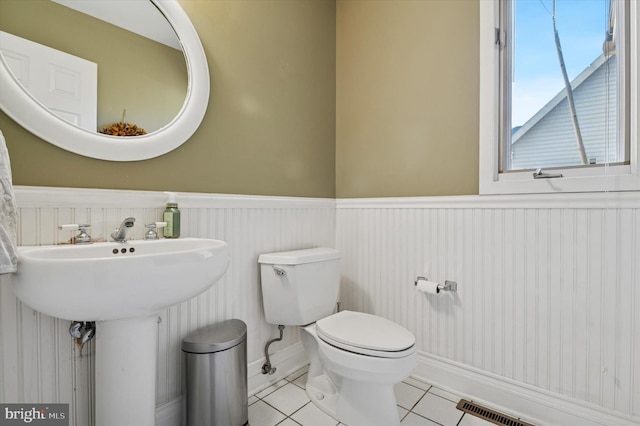 half bathroom with tile patterned floors, a wainscoted wall, toilet, and visible vents