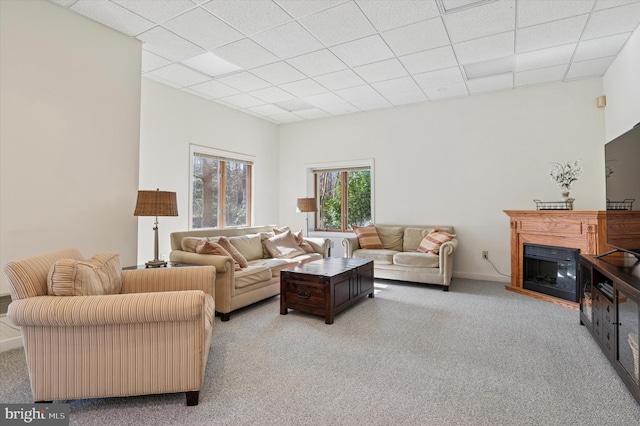 carpeted living room with a glass covered fireplace and a drop ceiling