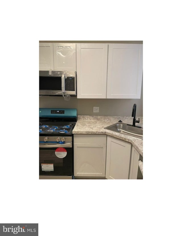 kitchen with white cabinetry, stainless steel appliances, light countertops, and a sink