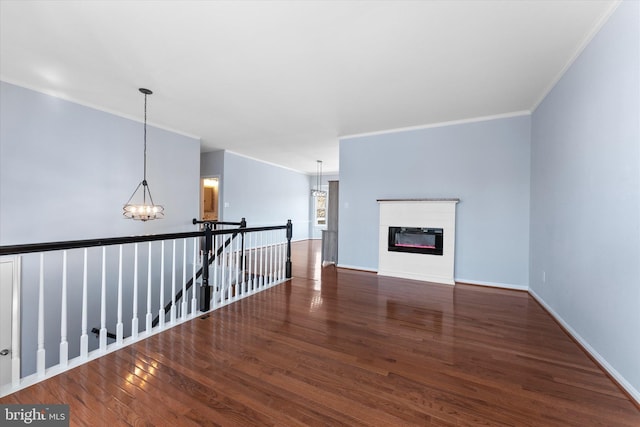 unfurnished living room with wood finished floors, baseboards, ornamental molding, a glass covered fireplace, and a chandelier