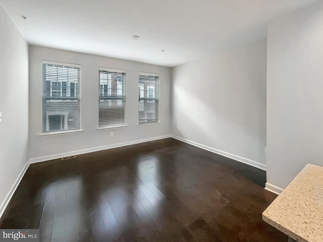 empty room with dark wood-type flooring, visible vents, and baseboards