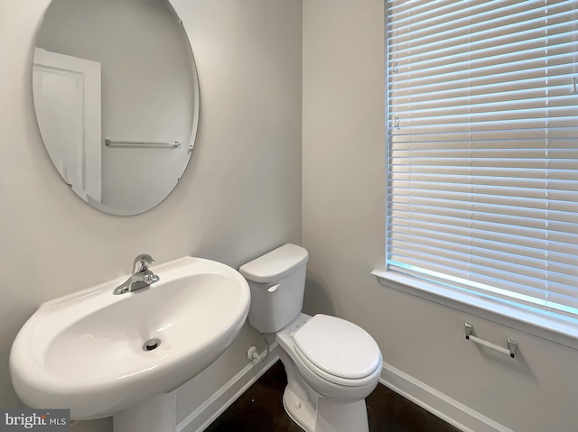 half bathroom featuring toilet, baseboards, and a sink