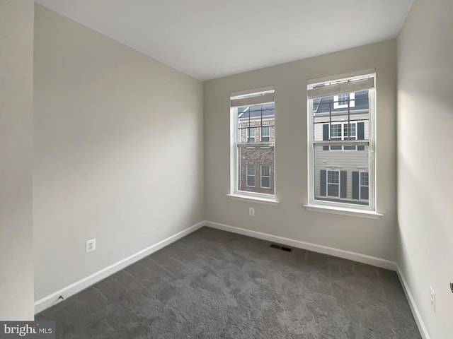 empty room with visible vents, baseboards, and dark carpet