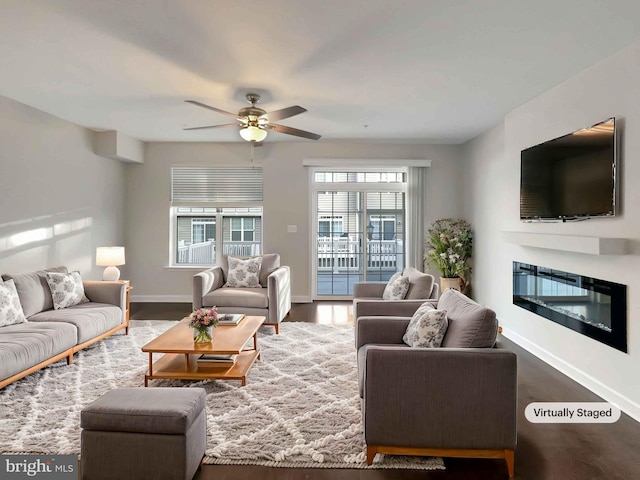 living room featuring ceiling fan, baseboards, wood finished floors, and a glass covered fireplace