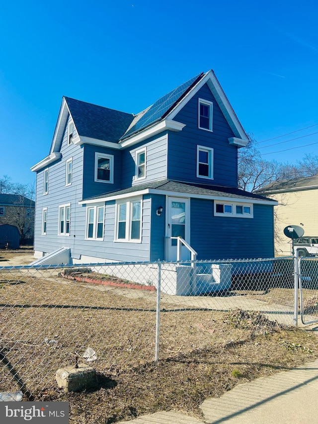 view of front of property featuring a fenced front yard, solar panels, and a shingled roof