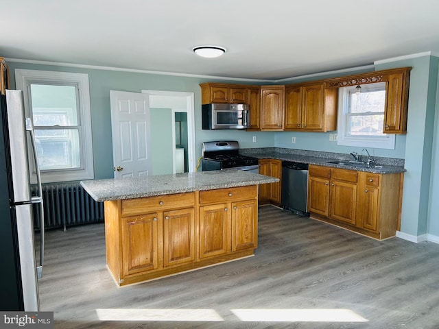 kitchen with radiator, brown cabinets, appliances with stainless steel finishes, light wood-style flooring, and a sink