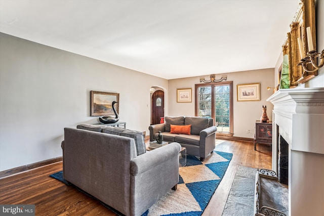 living area featuring arched walkways, a fireplace with flush hearth, baseboards, and wood finished floors