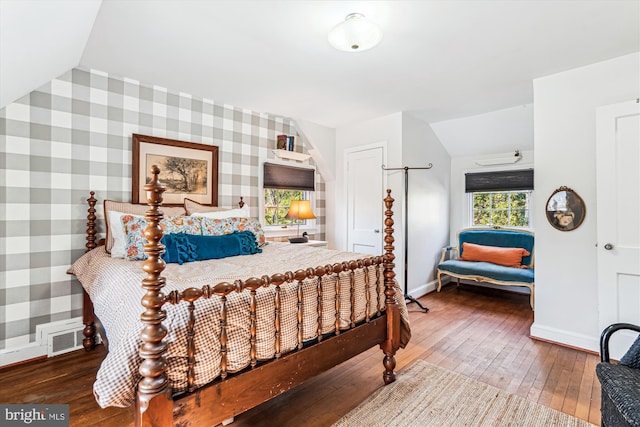 bedroom featuring visible vents, baseboards, wallpapered walls, hardwood / wood-style flooring, and an accent wall