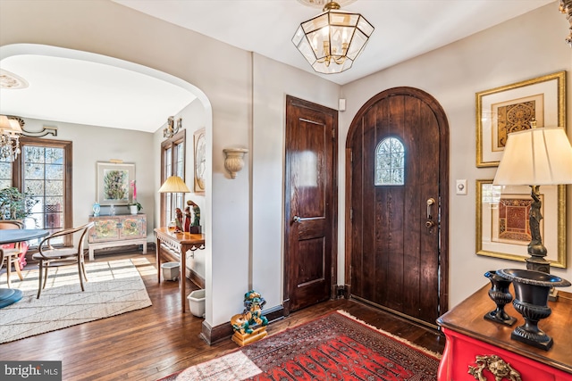 foyer entrance featuring baseboards, arched walkways, dark wood-type flooring, and an inviting chandelier