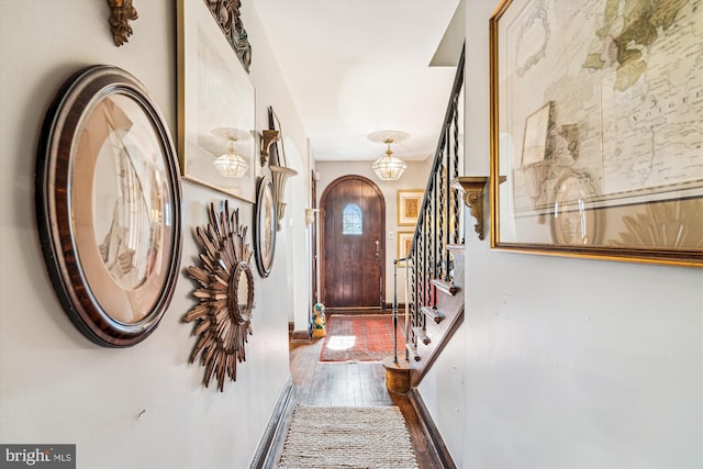 foyer entrance featuring arched walkways, stairs, baseboards, and wood finished floors