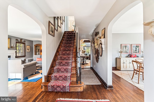 staircase with wood finished floors, arched walkways, and baseboards