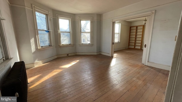 empty room featuring baseboards, radiator heating unit, and light wood finished floors