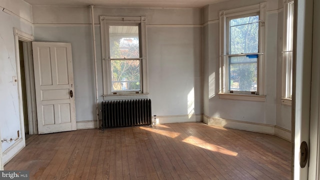 unfurnished room featuring a wealth of natural light, radiator, baseboards, and hardwood / wood-style floors