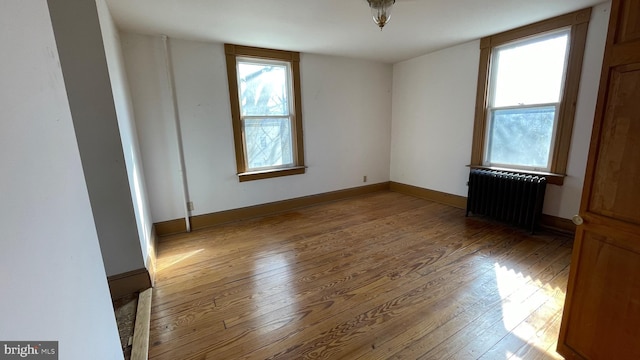 unfurnished bedroom featuring multiple windows, radiator heating unit, baseboards, and hardwood / wood-style flooring