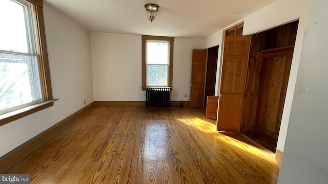 unfurnished bedroom with hardwood / wood-style floors, multiple windows, radiator heating unit, and baseboards